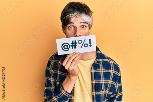Young hispanic man covering mouth with insult message paper scared and amazed with open mouth for surprise, disbelief face