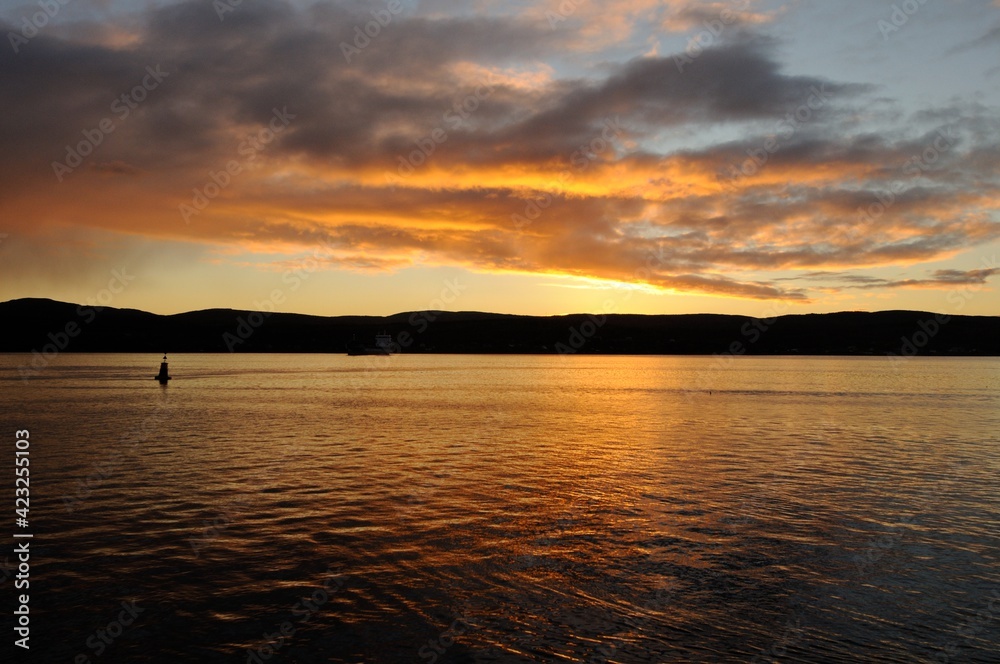 Obraz premium Autumn sunset in the city of Murmansk, late September. Dark mountains above the water, sunset, reflected in the water. Lonely buoy in the water. Murmansk region, Russia.