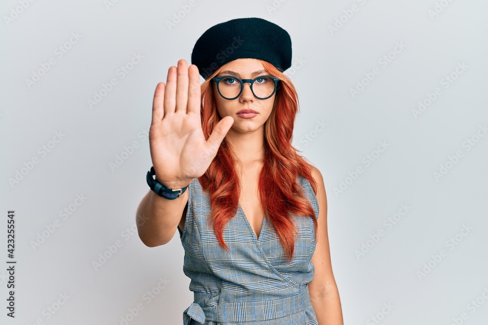 Young redhead woman wearing fashion french look with beret doing stop sing with palm of the hand. warning expression with negative and serious gesture on the face.