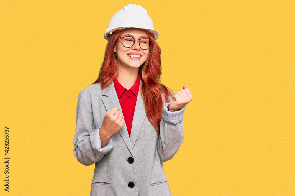 Young redhead woman wearing architect hardhat excited for success with arms raised and eyes closed celebrating victory smiling. winner concept.