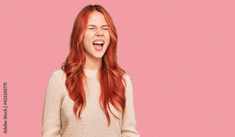 Obraz premium Young redhead woman wearing casual winter sweater angry and mad screaming frustrated and furious, shouting with anger. rage and aggressive concept.