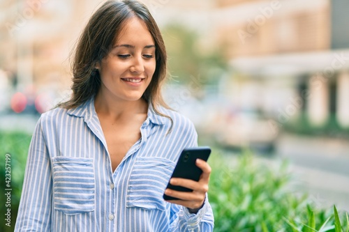 Young hispanic woman smiling happy using smartphone at the city.