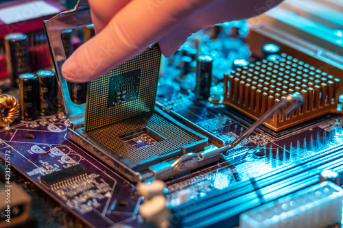 Engineer's gloved hand is holding the CPU chip on the background of the motherboard. High-tech hardware microelectronics photo