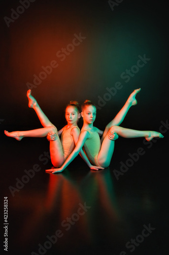 Fototapeta Naklejka Na Ścianę i Meble -  Touch. Two young gymnasts together in neon colored lights on a black background. The concept of gymnastics and modern choreography. Creative art photo.