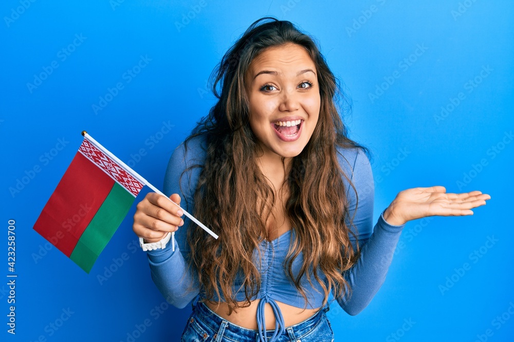 Young hispanic girl holding belarus flag celebrating achievement with happy smile and winner expression with raised hand Young hispanic girl holding belarus flag celebrating achievement with happy smile and winner expression with raised hand