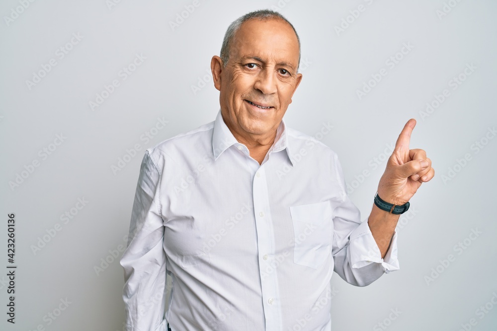 Handsome senior man wearing casual white shirt with a big smile on face, pointing with hand finger to the side looking at the camera. Handsome senior man wearing casual white shirt with a big smile on face, pointing with hand finger to the side looking at the camera.