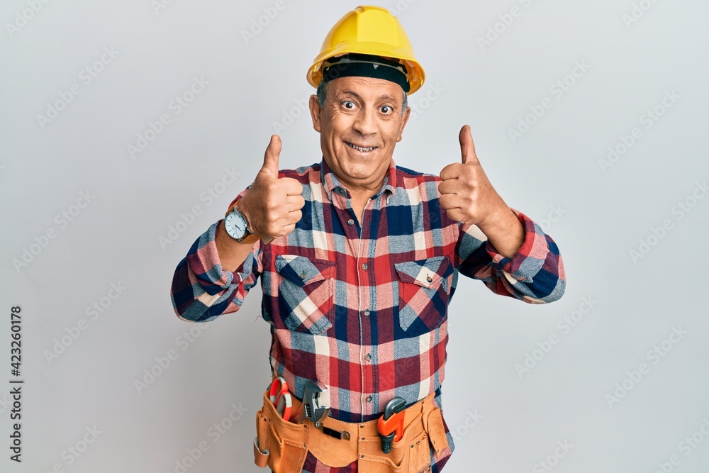 Senior hispanic man wearing handyman uniform success sign doing positive gesture with hand, thumbs up smiling and happy. cheerful expression and winner gesture.