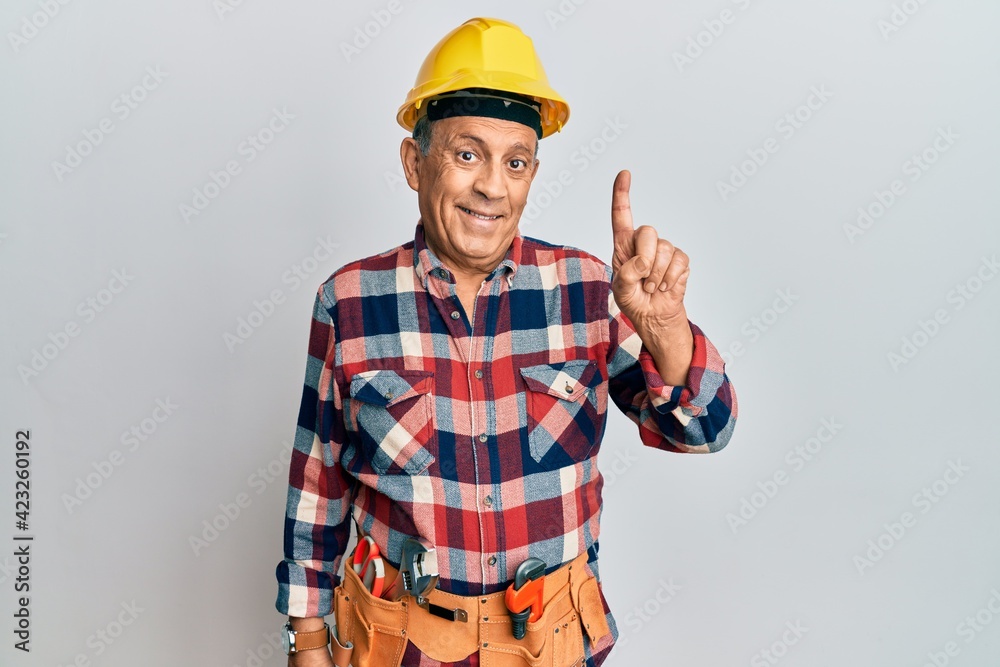 Senior hispanic man wearing handyman uniform showing and pointing up with finger number one while smiling confident and happy.