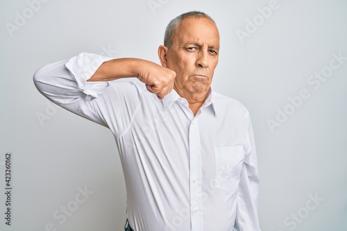 Handsome senior man wearing casual white shirt strong person showing arm muscle, confident and proud of power © Krakenimages.com