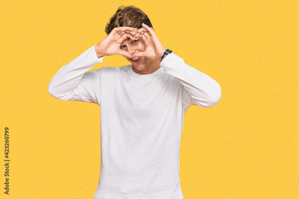 Handsome caucasian man wearing casual white sweater doing heart shape with hand and fingers smiling looking through sign Handsome caucasian man wearing casual white sweater doing heart shape with hand and fingers smiling looking through sign