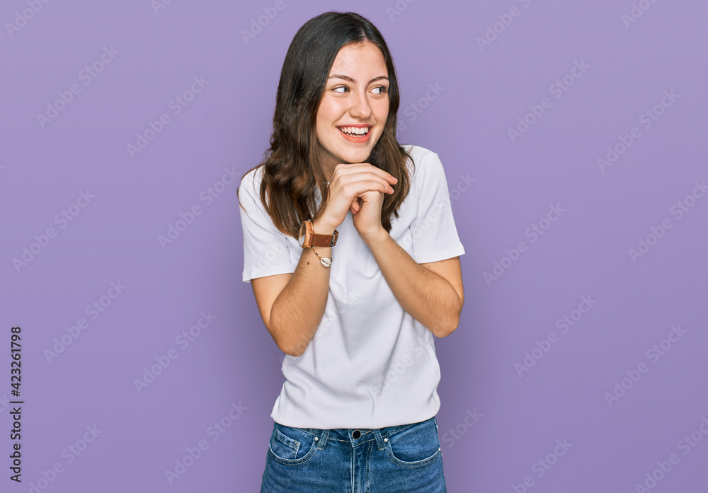 Young beautiful woman wearing casual white t shirt laughing nervous and excited with hands on chin looking to the side Young beautiful woman wearing casual white t shirt laughing nervous and excited with hands on chin looking to the side