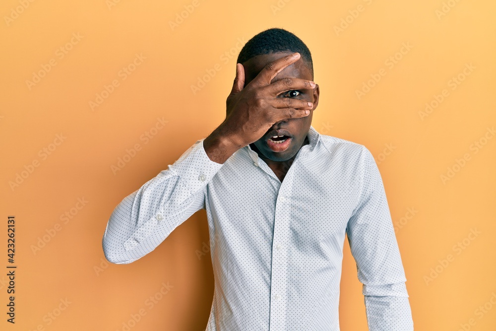 Young african american man wearing casual clothes peeking in shock covering face and eyes with hand, looking through fingers afraid Young african american man wearing casual clothes peeking in shock covering face and eyes with hand, looking through fingers afraid
