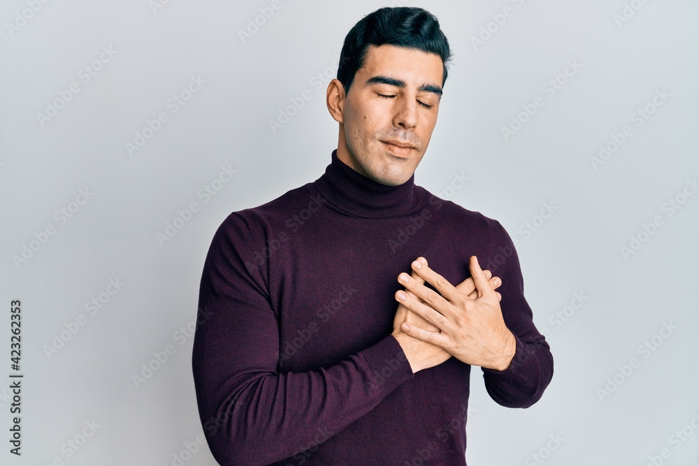 Handsome hispanic man wearing turtleneck sweater smiling with hands on chest, eyes closed with grateful gesture on face. health concept. Handsome hispanic man wearing turtleneck sweater smiling with hands on chest, eyes closed with grateful gesture on face. health concept.