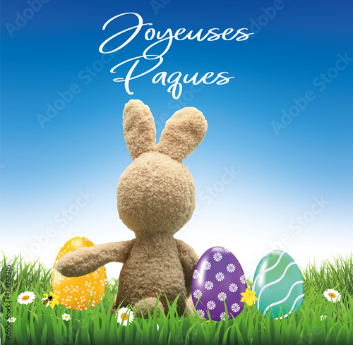 carte ou bandeau sur Joyeuses Pâques en blanc avec un lapin en peluche de dos et à coté 3 oeufs décorés  posés sur l'herbe sur un fond bleu et blanc en dégradé