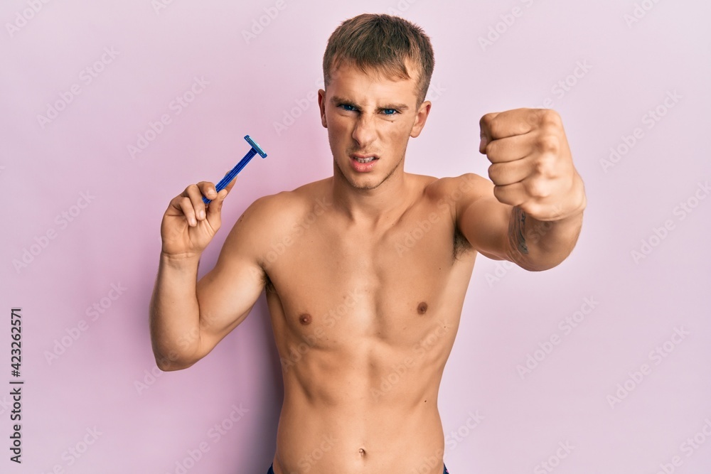 Young caucasian man shirtless holding razor annoyed and frustrated shouting with anger, yelling crazy with anger and hand raised Young caucasian man shirtless holding razor annoyed and frustrated shouting with anger, yelling crazy with anger and hand raised