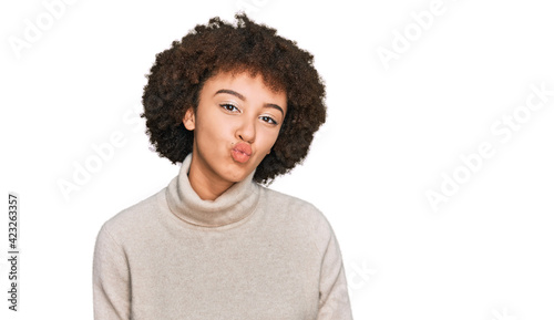 Young hispanic girl wearing wool winter sweater looking at the camera blowing a kiss on air being lovely and sexy. love expression.