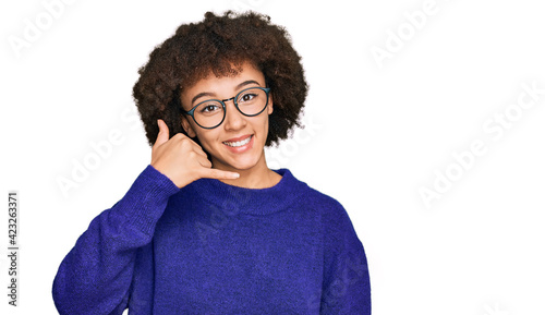 Young hispanic girl wearing casual winter sweater and glasses smiling doing phone gesture with hand and fingers like talking on the telephone. communicating concepts.