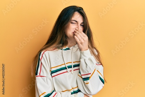 Young caucasian woman wearing casual clothes smelling something stinky and disgusting, intolerable smell, holding breath with fingers on nose. bad smell