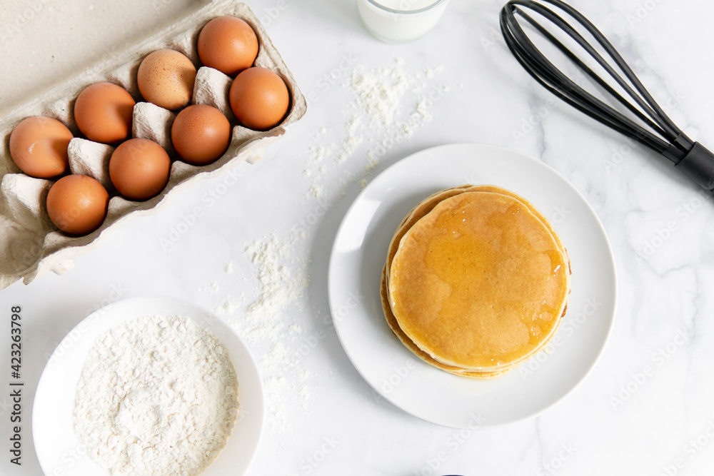 composition of small desserts for baking. eggs, muffins, flour, milk, whisk and spoon on a light background. Close-up of baked pancakes on a white plate. composition of small desserts for baking. eggs, muffins, flour, milk, whisk and spoon on a light background. Close-up of baked pancakes on a white plate.