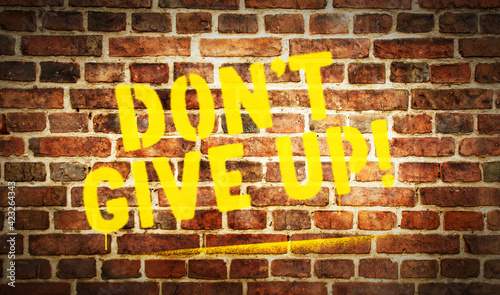 Don't give up sign spray painted on the brick wall © PerlaStudio