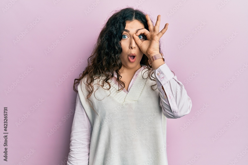 Young brunette woman with curly hair wearing casual clothes doing ok gesture shocked with surprised face, eye looking through fingers. unbelieving expression. Young brunette woman with curly hair wearing casual clothes doing ok gesture shocked with surprised face, eye looking through fingers. unbelieving expression.