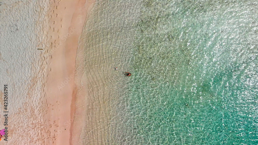 Young girl enjoying a beautiful beach shoreline. Crystal clear ocean water, downward view from drone