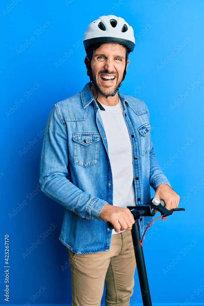 Young handsome man standing on modern scooter wearing helmet smiling and laughing hard out loud because funny crazy joke. Young handsome man standing on modern scooter wearing helmet smiling and laughing hard out loud because funny crazy joke.