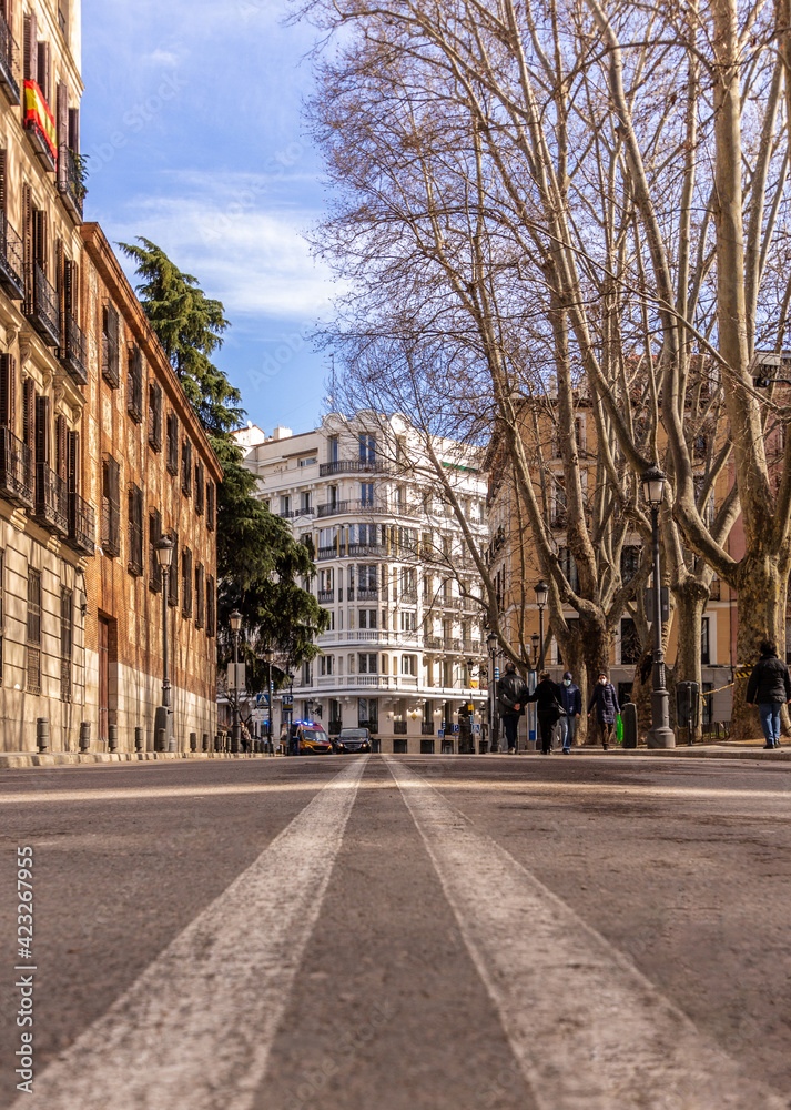 Ground level point of view of a road in Madrid, with a white building at the end of the street.