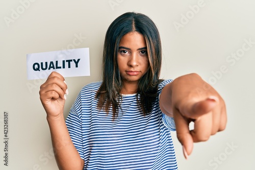 Εκτύπωση καμβά Young latin girl holding quality word on paper pointing with finger to the camer