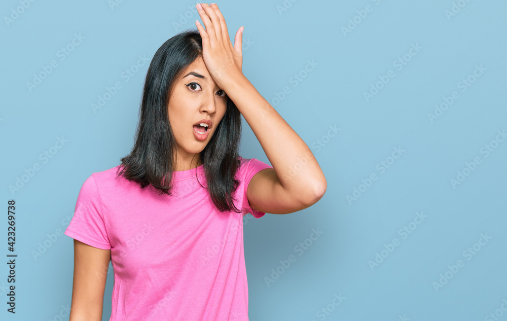 Beautiful asian young woman wearing casual pink t shirt surprised with hand on head for mistake, remember error. forgot, bad memory concept.