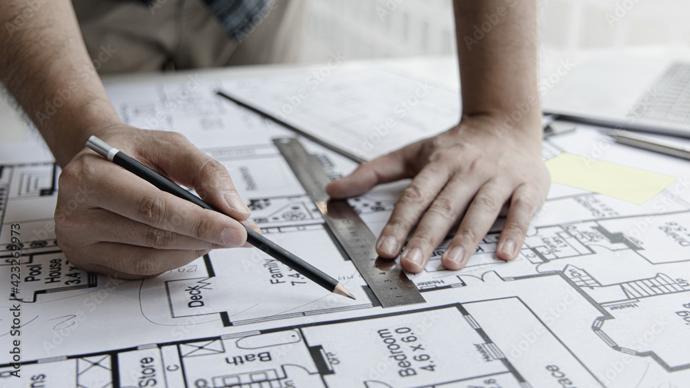 Architectural building design and construction plans with blueprints, Young man was designing a building or architecture with a ruler, pen, pencil, tape measure, architect hat and other equipment. Architectural building design and construction plans with blueprints, Young man was designing a building or architecture with a ruler, pen, pencil, tape measure, architect hat and other equipment.