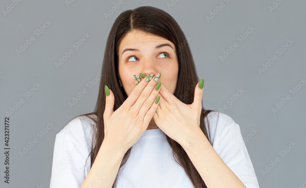 Pretty young female in white T-shirt covering mouth with hands and cheerfully laughing at joke while standing against gray background Pretty young female in white T-shirt covering mouth with hands and cheerfully laughing at joke while standing against gray background