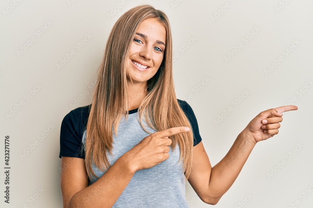 Young blonde woman wearing casual clothes smiling and looking at the camera pointing with two hands and fingers to the side. Young blonde woman wearing casual clothes smiling and looking at the camera pointing with two hands and fingers to the side.