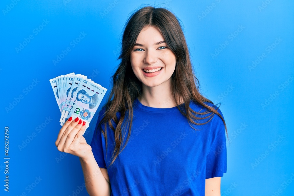 Young beautiful caucasian girl holding 10 yuan chinese banknotes looking positive and happy standing and smiling with a confident smile showing teeth Young beautiful caucasian girl holding 10 yuan chinese banknotes looking positive and happy standing and smiling with a confident smile showing teeth