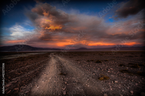 A rocky and dusty road winds its way down the high desert in SW Bolivia leading your eyes to a dramatic sunset.   