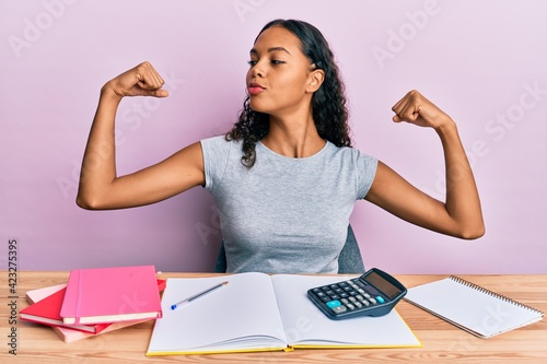 Young african american girl accountant working at the office showing arms muscles smiling proud. fitness concept.