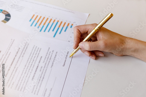 Young business woman signs a business contract on the background of economic charts while sitting at the table. Business and finance concept. Selective focus.