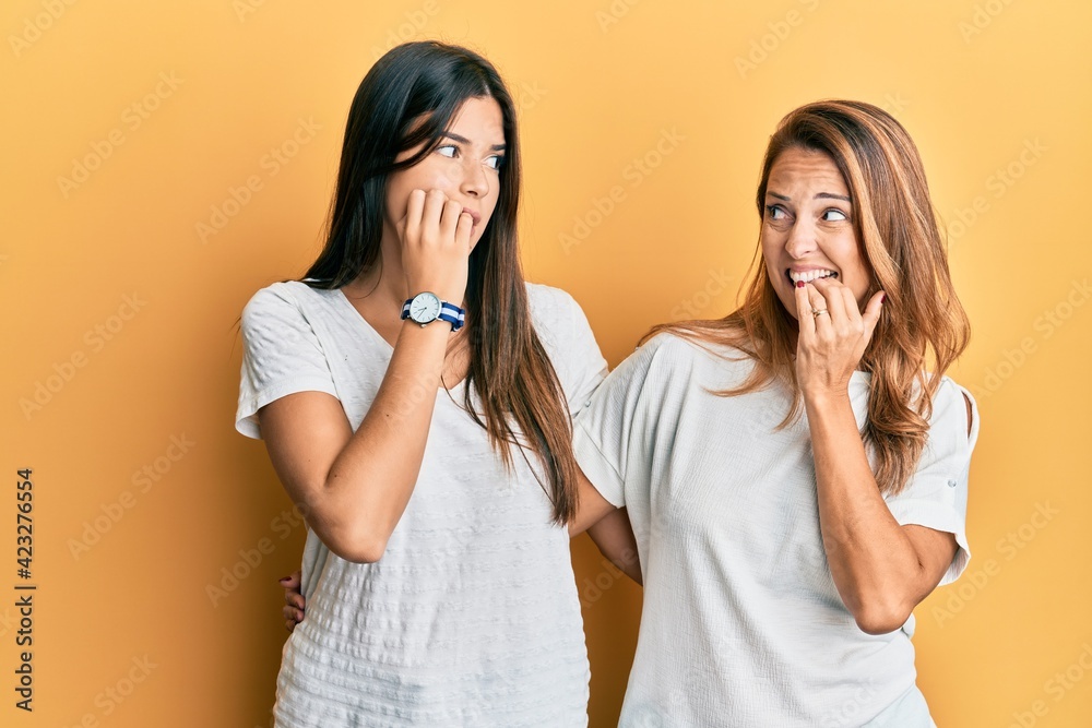 Hispanic family of mother and daughter wearing casual white tshirt looking stressed and nervous with hands on mouth biting nails. anxiety problem. Hispanic family of mother and daughter wearing casual white tshirt looking stressed and nervous with hands on mouth biting nails. anxiety problem.