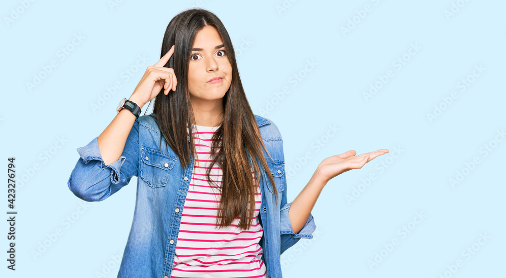 Young brunette woman wearing casual clothes confused and annoyed with open palm showing copy space and pointing finger to forehead. think about it. Young brunette woman wearing casual clothes confused and annoyed with open palm showing copy space and pointing finger to forehead. think about it.