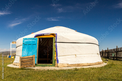 Beautiful traditional Mongolian white Yurt with blue door, on green grass and very blue sky © vladimir