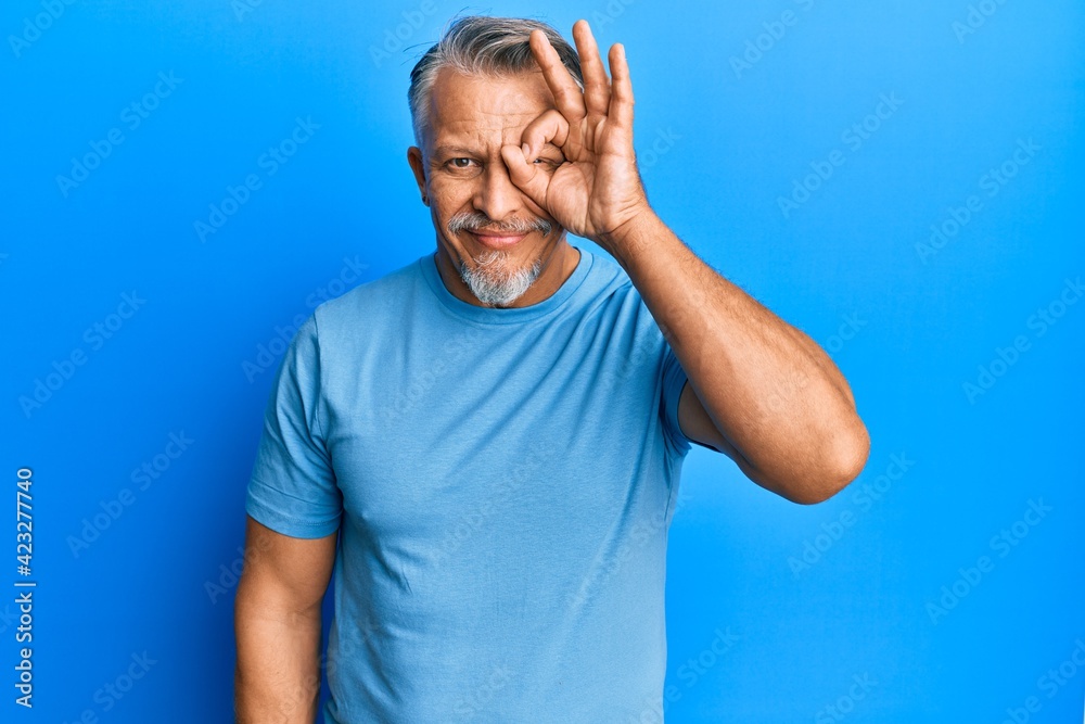 Naklejka premium Middle age grey-haired man wearing casual clothes doing ok gesture with hand smiling, eye looking through fingers with happy face.