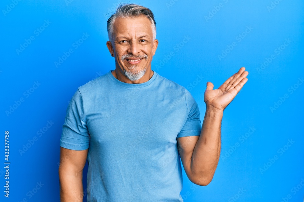 Middle age grey-haired man wearing casual clothes smiling cheerful presenting and pointing with palm of hand looking at the camera. Middle age grey-haired man wearing casual clothes smiling cheerful presenting and pointing with palm of hand looking at the camera.