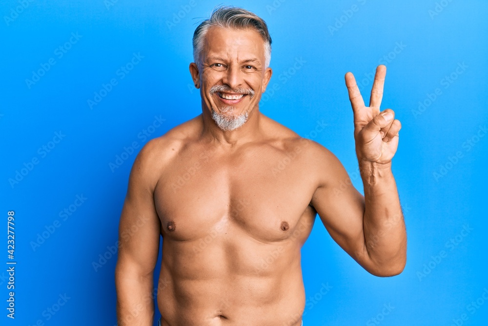 Fototapeta premium Middle age grey-haired man standing shirtless showing and pointing up with fingers number two while smiling confident and happy.