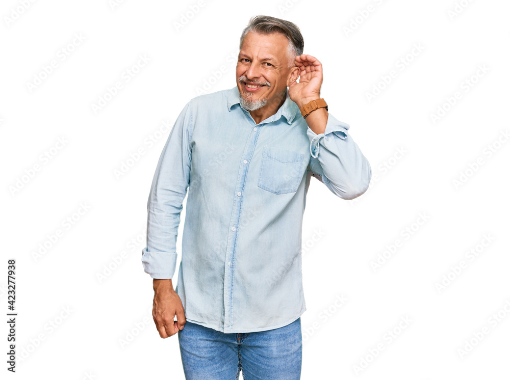 Middle age grey-haired man wearing casual clothes smiling with hand over ear listening an hearing to rumor or gossip. deafness concept. Middle age grey-haired man wearing casual clothes smiling with hand over ear listening an hearing to rumor or gossip. deafness concept.