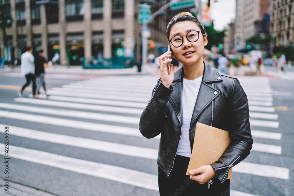 Millennial female student in classic spectacles making consultancy roaming conversation via cellphone app, Asian tourist with education textbook for sketches phoning for discuss vacations time