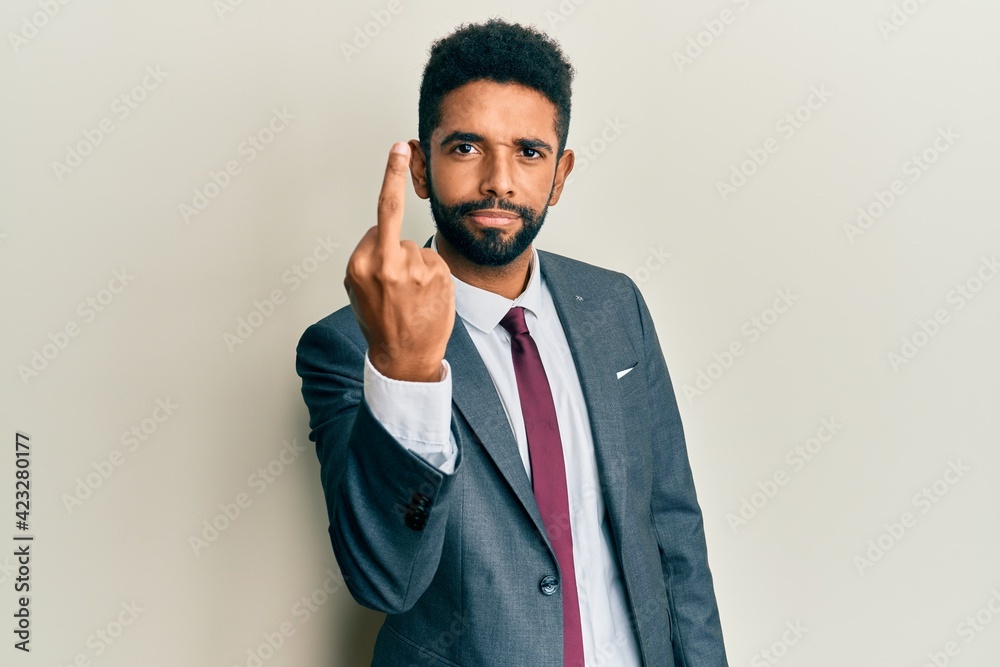 Handsome hispanic man with beard wearing business suit and tie showing middle finger, impolite and rude fuck off expression Handsome hispanic man with beard wearing business suit and tie showing middle finger, impolite and rude fuck off expression