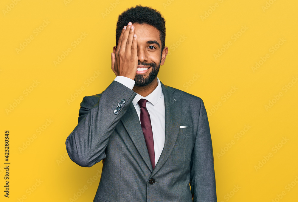 Young african american man wearing business clothes covering one eye with hand, confident smile on face and surprise emotion. Young african american man wearing business clothes covering one eye with hand, confident smile on face and surprise emotion.