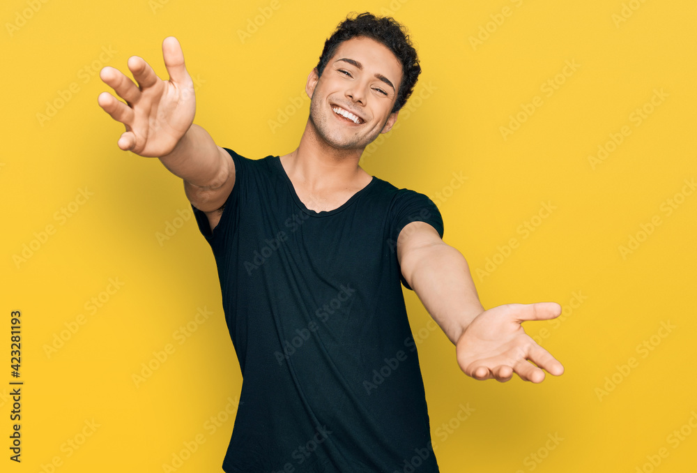 Young handsome man wearing casual black t shirt looking at the camera smiling with open arms for hug. cheerful expression embracing happiness. Young handsome man wearing casual black t shirt looking at the camera smiling with open arms for hug. cheerful expression embracing happiness.