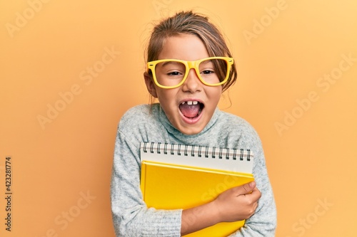 Little beautiful girl wearing glasses and holding books smiling and laughing hard out loud because funny crazy joke.