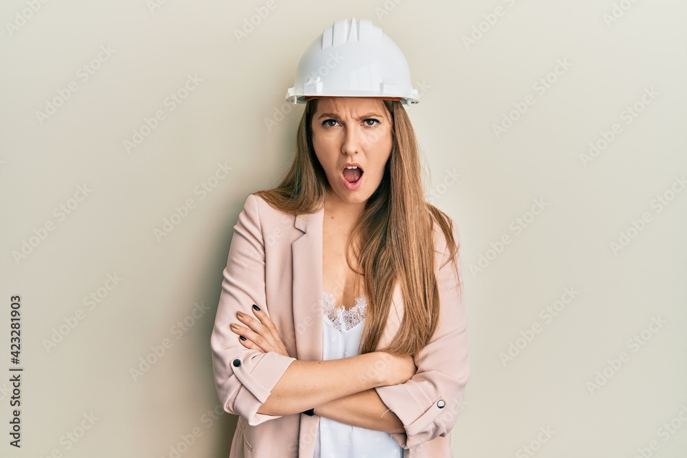 Young blonde woman wearing architect hardhat in shock face, looking skeptical and sarcastic, surprised with open mouth Young blonde woman wearing architect hardhat in shock face, looking skeptical and sarcastic, surprised with open mouth